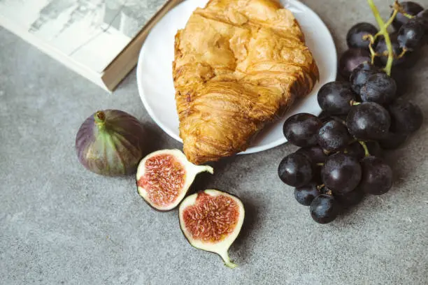 Een prachtige presentatie van een assortiment Franse kazen op een houten kaasplank, omringd door verse druiven, vijgen, noten en stokbrood. De diverse kazen variëren in kleur, textuur en smaak, en beloven een smaakvolle en gevarieerde ervaring.